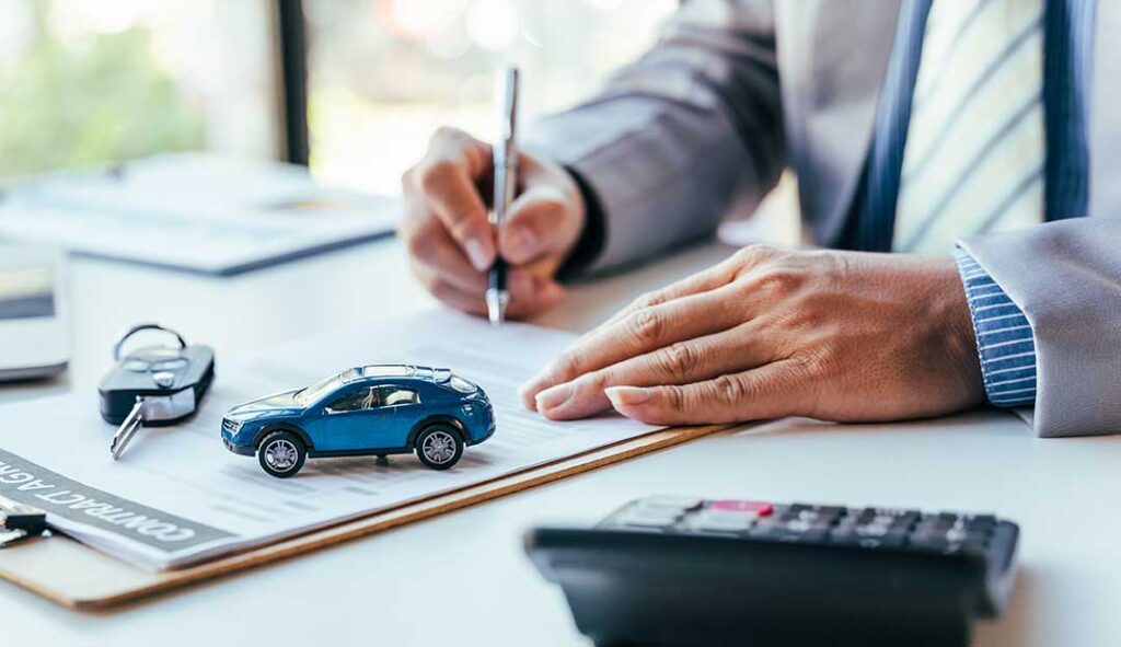A couple reviews insurance papers beside a new car parked in a residential driveway.