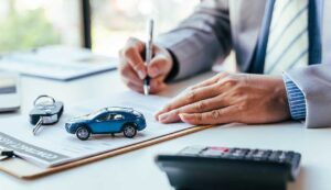 A couple reviews insurance papers beside a new car parked in a residential driveway.